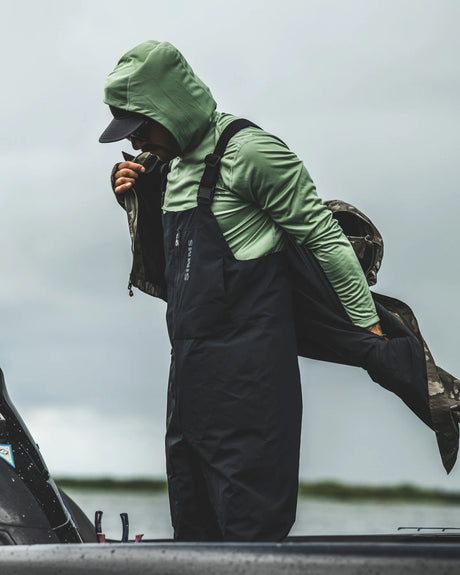 Person wearing green jacket and black rain pants on a boat