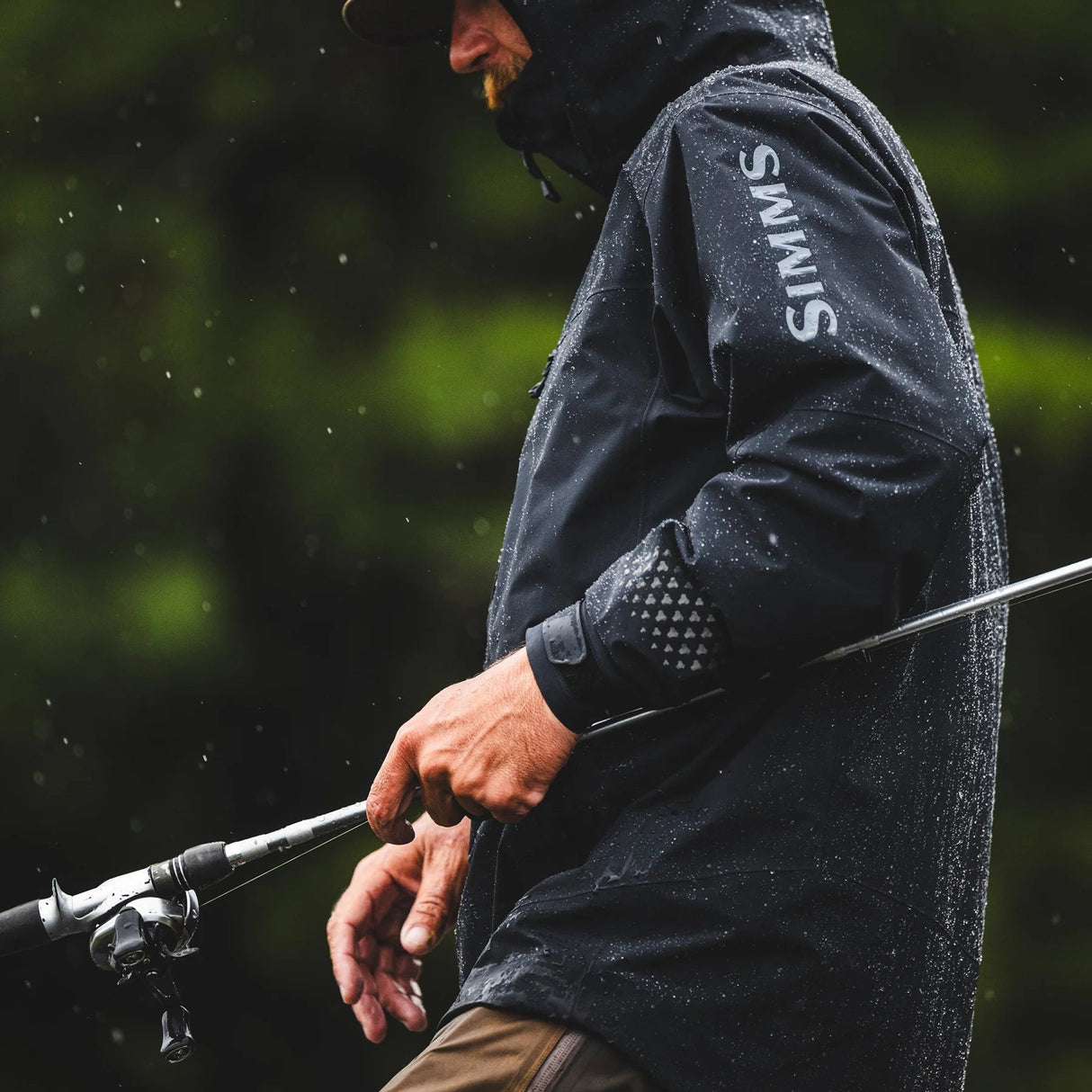 Angler fishing in the rain wearing a black SIMMS waterproof fishing jacket