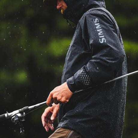 Angler fishing in the rain wearing a black SIMMS waterproof fishing jacket