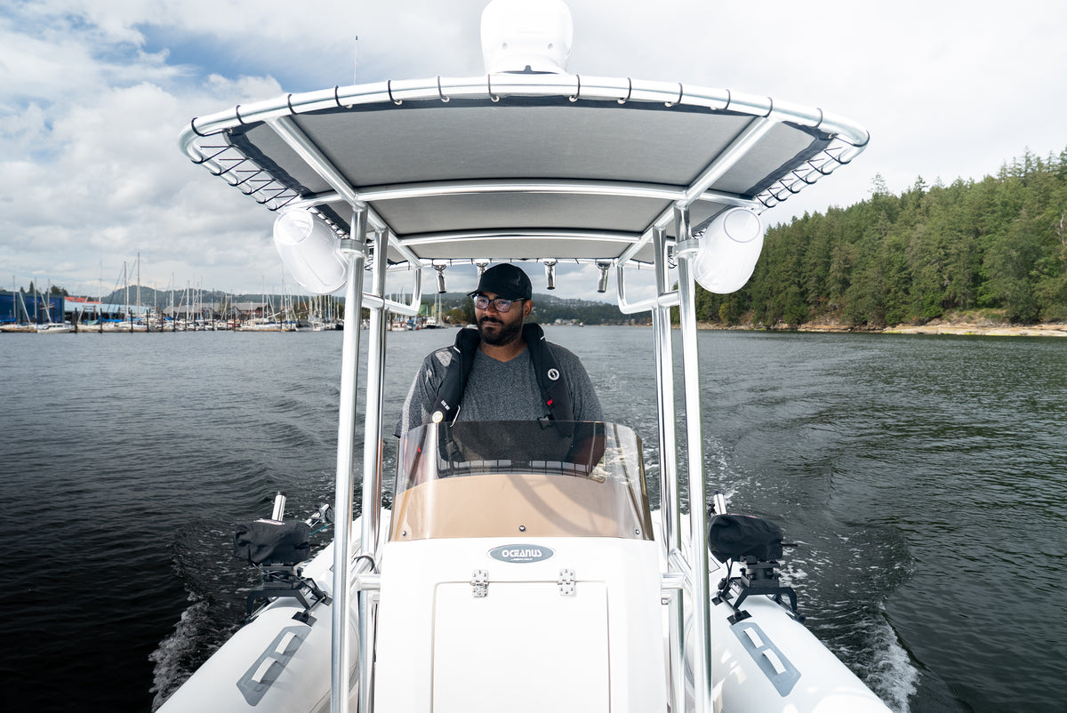 Skipper driving the AB Inflatables 21 Oceanus VST under the T-top, with a marina and forested shore behind