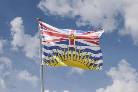 British Columbia flag flying on a flagpole against blue sky with clouds