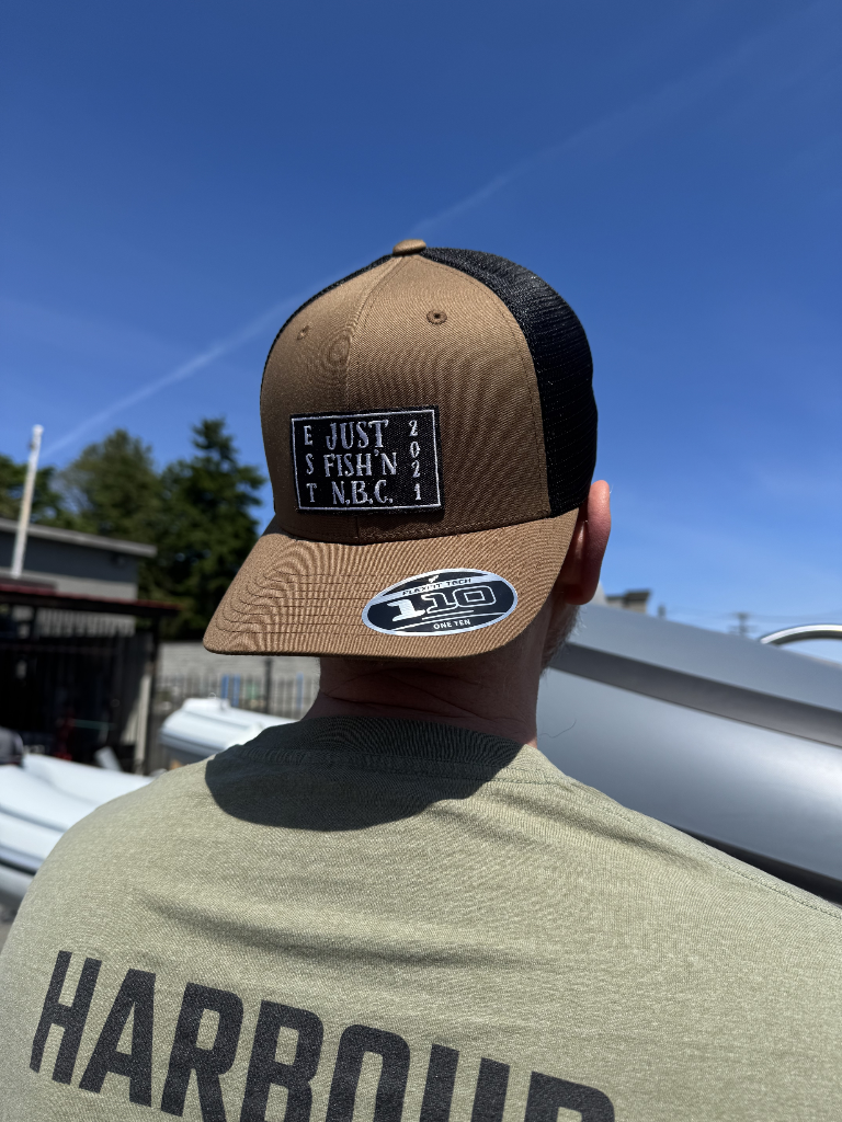 Person wearing a tan and black cap with a visible brand logo, standing outdoors with a clear blue sky.