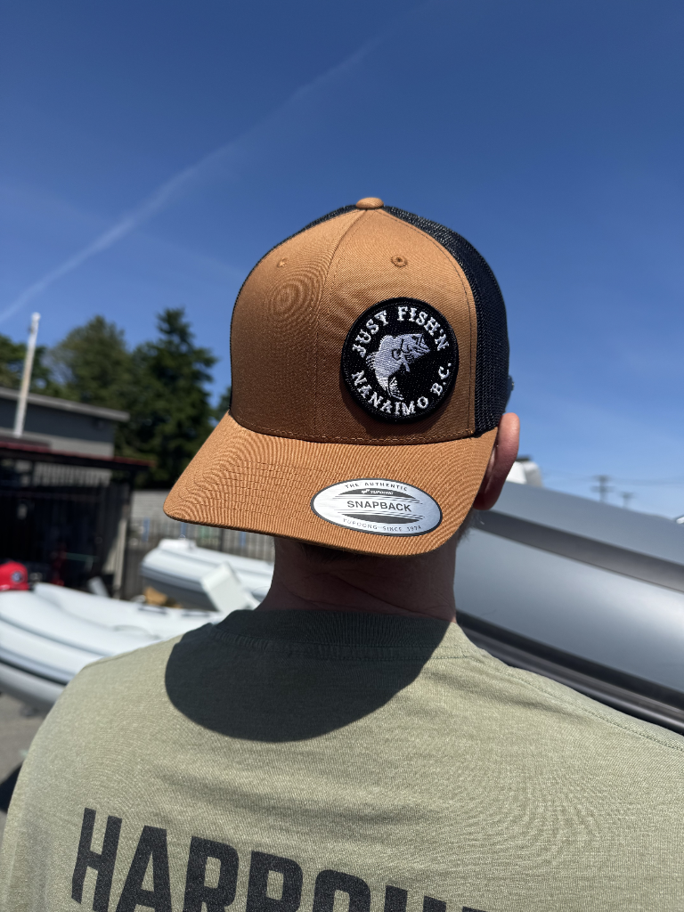 Person wearing a tan and black cap with a logo against a blue sky.