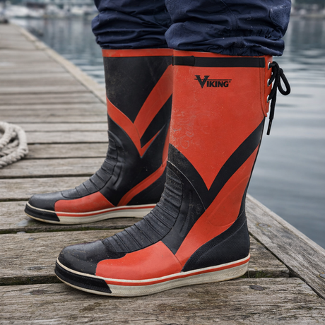Red Viking Mariner yacht boots worn on a weathered dock beside calm marina water showing real marine working conditions