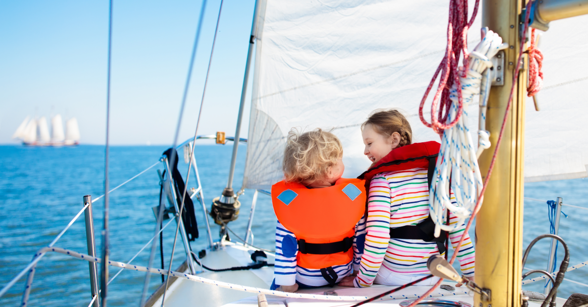 Children wearing bright orange and red life jackets on a sailboat – choosing the right flotation vests for boating safety.