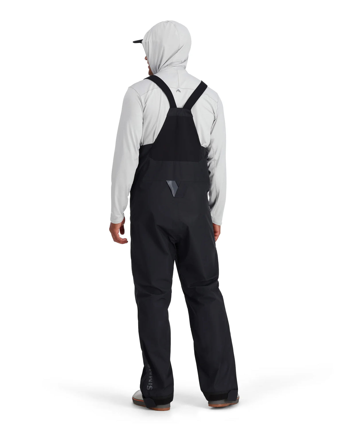 Person wearing a black bib overalls and light gray hoodie on a white background