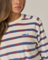A woman with long brown hair wears the Salty Crew Night N Day Crew in Off White, featuring red and blue terry stripes and a small blue fish logo with "Salty Crew" text on the chest. The background is plain and neutral.