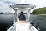 Skipper driving the AB Inflatables 21 Oceanus VST under the T-top, with a marina and forested shore behind