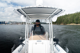 Skipper driving the AB Inflatables 21 Oceanus VST under the T-top, with a marina and forested shore behind