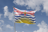 British Columbia flag flying on a flagpole against blue sky with clouds