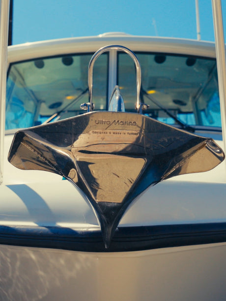 Bow of a cabin cruiser in a marina with a stainless anchor on the bow roller