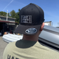 Person wearing a black cap with text and a green shirt with 'Harbour' text, outdoors.