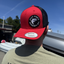 Person wearing a red and black cap with a logo, standing outdoors.