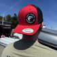Person wearing a red and black cap with a logo, standing outdoors.