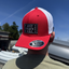 Red and white cap with a patch on a person against a blue sky.