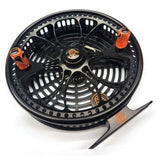 Black fly fishing reel with orange accents on a white background