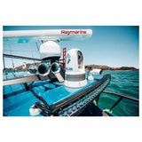 A Raymarine radar system mounted on a boat deck, featuring a white radar dome and a FLIR camera, set against a background of blue water and sky.